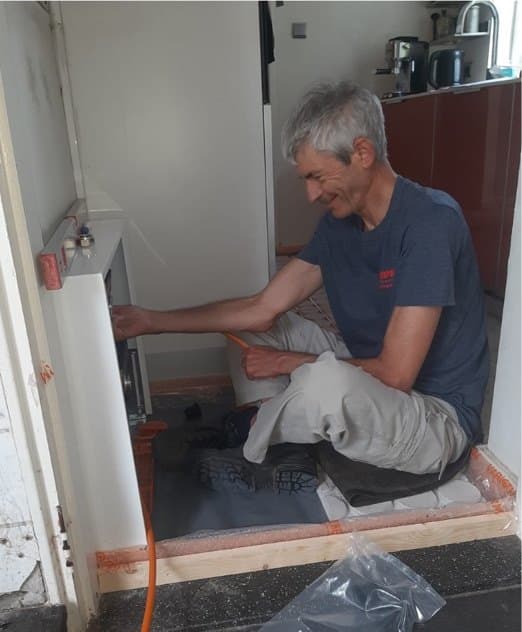 Michel maakt zittend de aansluiting van de vloerverwarming op de verdeler in gereedheid