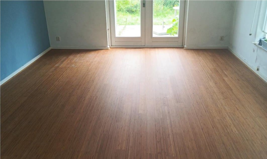 Woonkamer met een afgewerkte bamboevloer waaronder de vloerverwarming ligt, met openslaande deuren naar de tuin